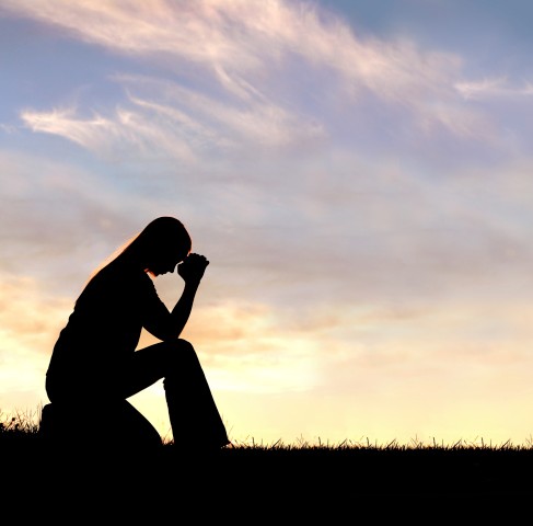 The silhouette of a woman praying at dawn