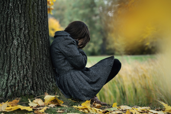 An unhappy woman leans against a tree, crying
