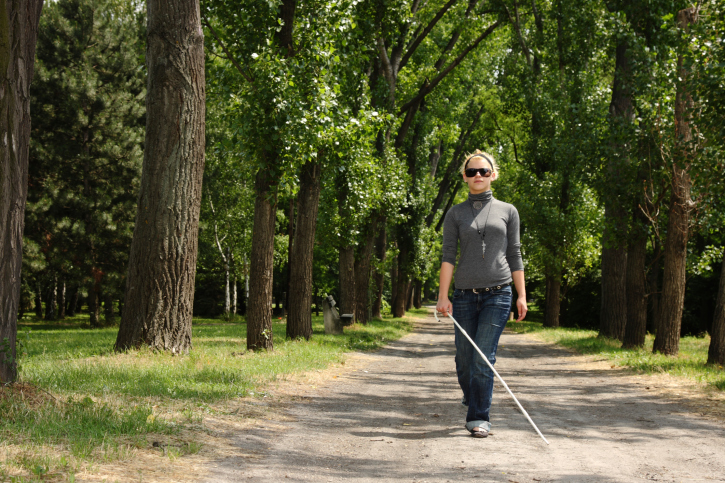A blind woman walks through a park