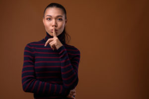 Person in turtleneck with long ponytail holds finger to lips