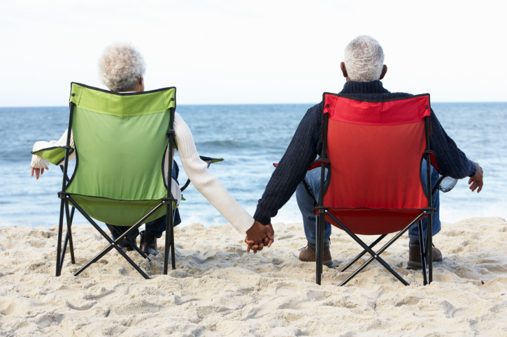 A senior couple holding hands watches the sea