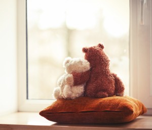 Two embracing loving teddy bear toys sitting on window-sill