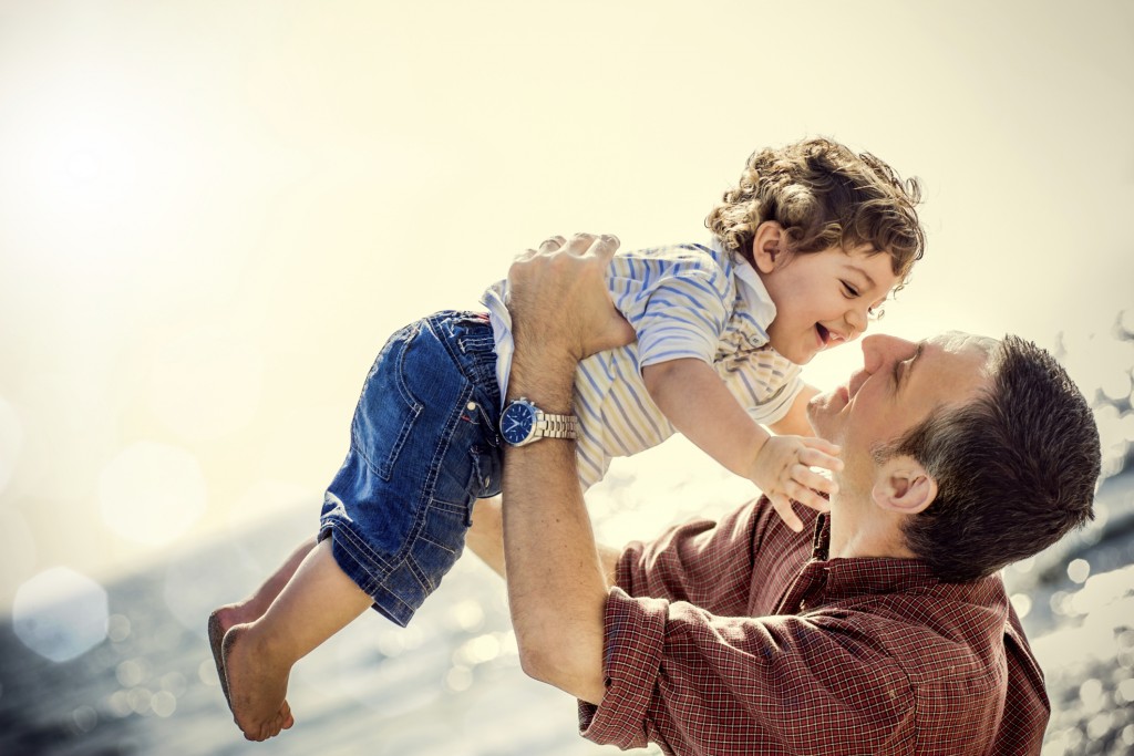 A smiling father holds his son up in the air