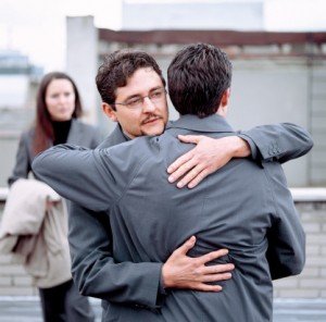 close-up of two men hugging with a woman standing behind them