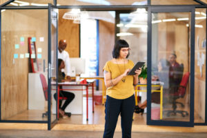 Young adult with shoulder-length hair and tattoos works in office using tablet 