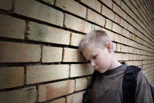 Forlorn boy leans his head against a brick wall