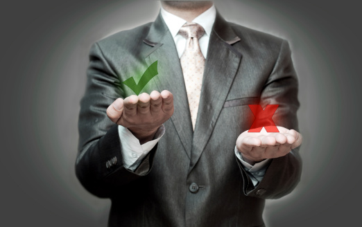 Man in suit holds right and wrong symbols in hands