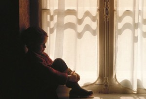 Boy (6-7) sitting by closed door, side view