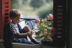 Boy (4-5) sitting on window sill, side view