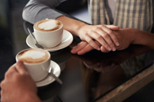 Cropped shot of a couple in a coffee shop, focus on hands and cups of coffee on table
