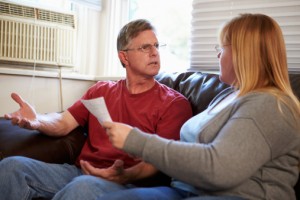 Worried Couple Sitting On Sofa Arguing About Bills