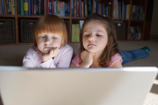 Young girls (5-6) lying on floor using laptop,  contemplating with hand on chin