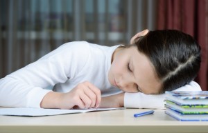 Child working on schoolwork with head on desk