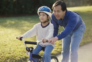 A man helps a young boy ride a bicycle