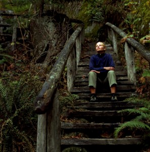 Young woman in forest, sitting on wooden staircase, looking upward