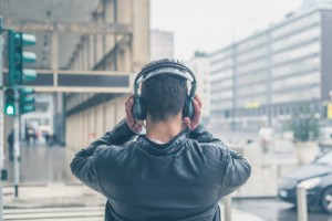 Rear view of man holding and listening to headphones in city