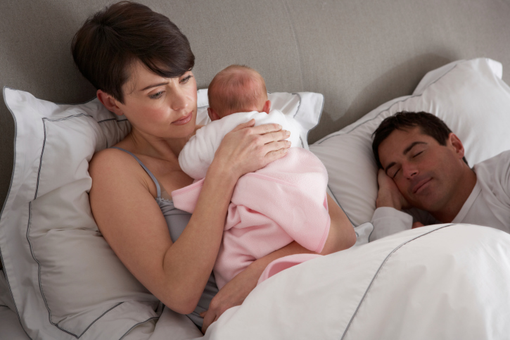Mother cuddles a newborn baby in bed while the father sleeps