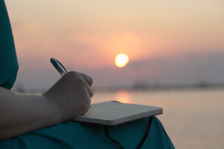 A woman writes in her journal outside at sunsey