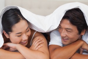 Happy couple lying on bed together under the duvet