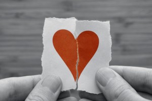 Man holds red broken paper heart in his hands