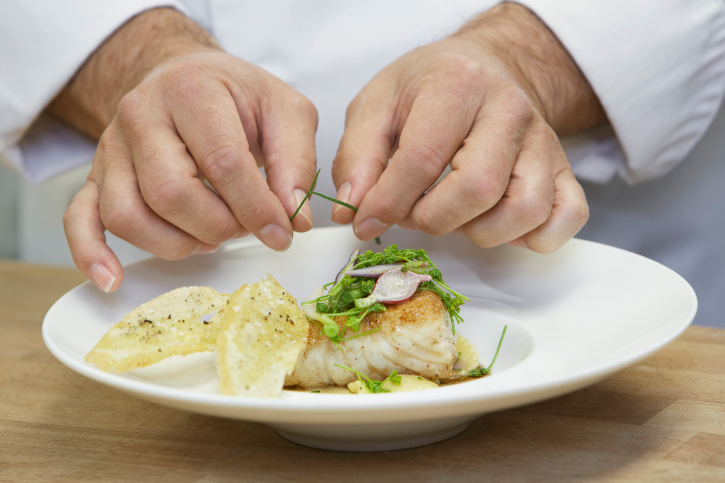 Hands garnishing fish course on plate