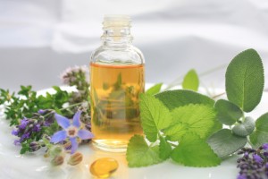 Fresh herbs lying next to a glass bottle of essential oils