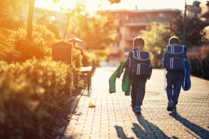 Rear view photo of two children walking home from school wearing backpacks and carrying jackets