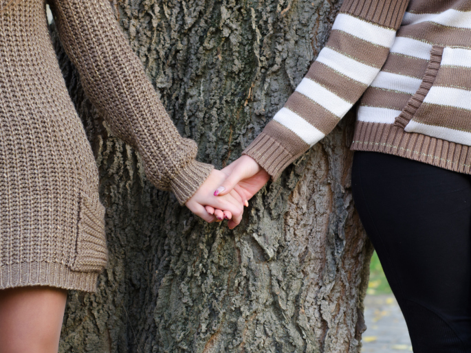 Same-sex couple holding hands against a tree