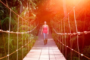 Happy woman hiker crossing suspension bridge in sunlight.
