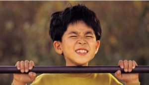 Young child with short, tousled hair has intense expression of concentration while doing chin-up on purple bar