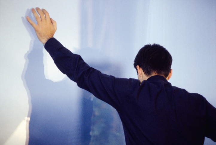 Young man standing against wall, rear view
