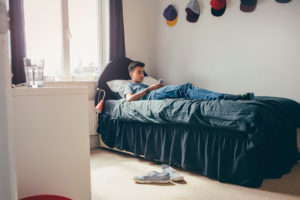 Teenage boy lying on his bed at home using a smartphone to text