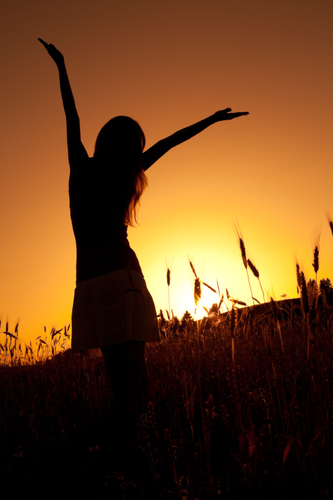 Standing on hill raising arms at sunset