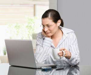 Woman holding mug and working with laptop
