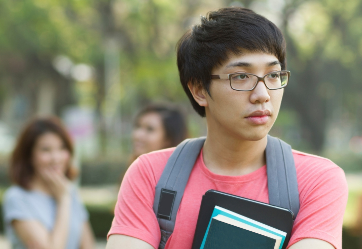 Young man looks away as girls talk behind him