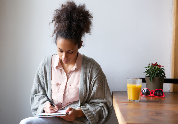 Young woman sitting at table writing in notepad