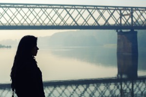 A woman stands alone in front of a bridge