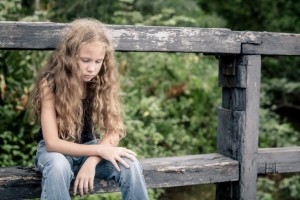 Downcast girl sitting on fence