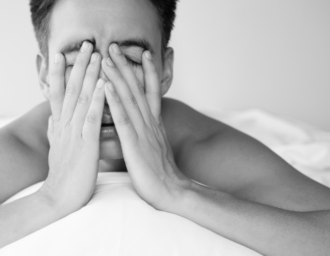 Man in bed rubs eyes with hands