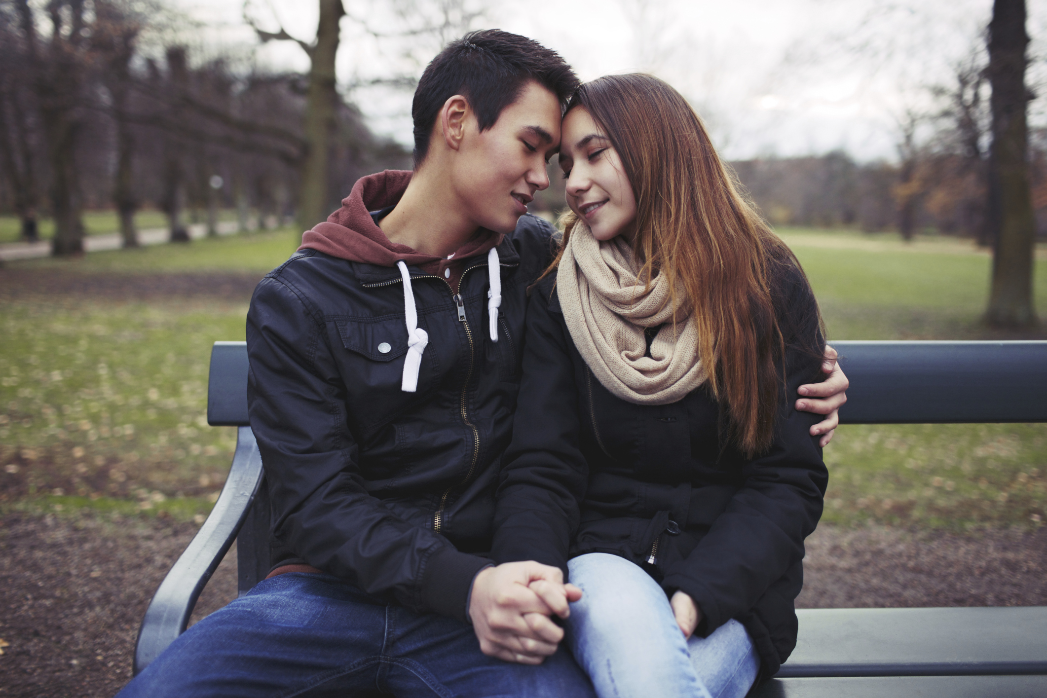 Teen couple holding hands and cuddling on bench