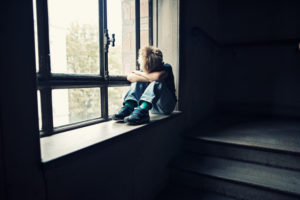Young child sitting alone in window with head down 