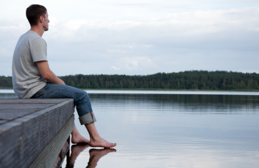 A young man sitting alone by the water