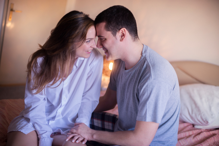 Couple with foreheads touching sitting on bed