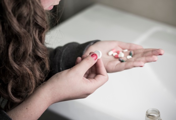 Girl holding several different pills in her hand