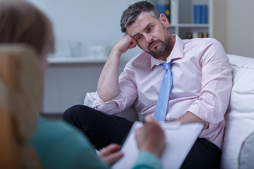 Man in therapy rests head on hand with blank expression