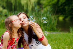 Mother and little girl blowing bubbles in park