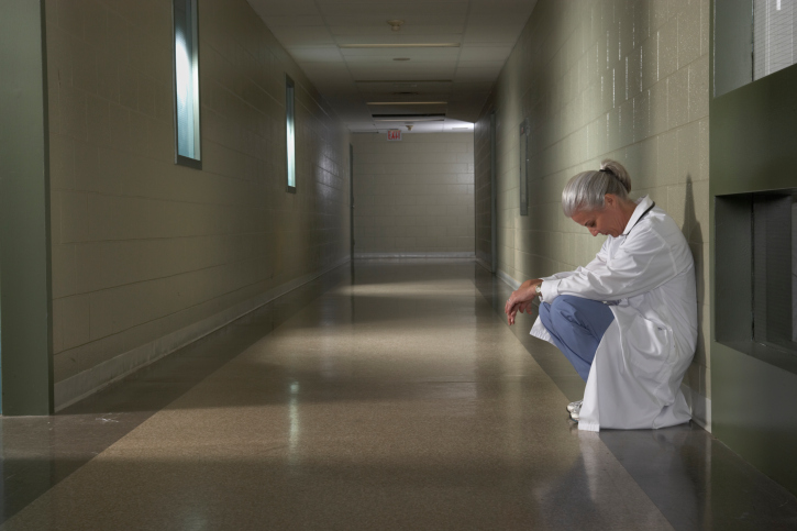 Doctor sitting alone in hallway with head down