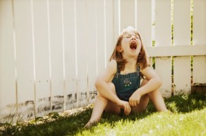 Young child sits in grass by fence and screams