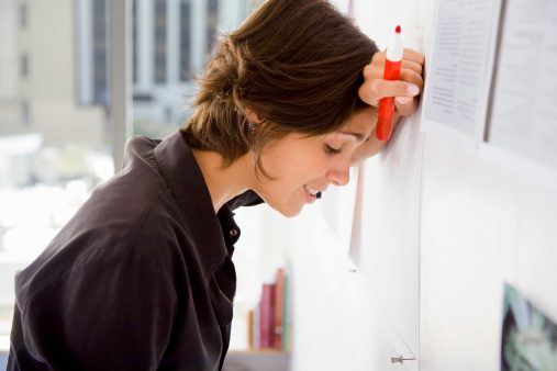 Woman with marker leans head against whiteboard