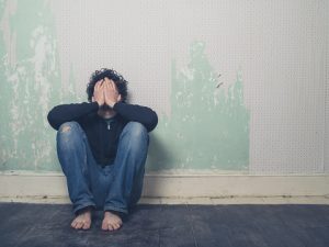 Young man sitting against wall with hands over face